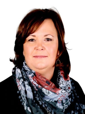 A woman with brown hair and a colorful floral scarf smiles gently while looking forward against a plain white background.