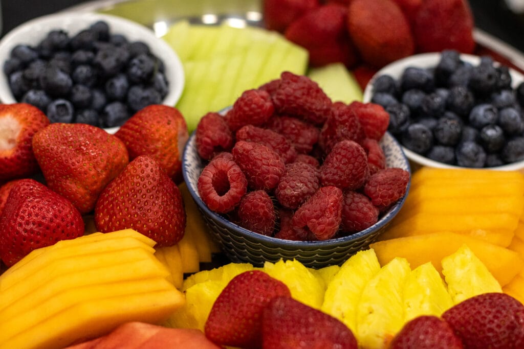 A vibrant array of fresh strawberries, blueberries, raspberries, melon, mango, and pineapple is arranged on a platter.